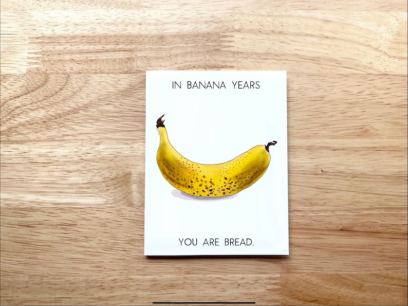 May include: A white card with the text "In Banana Years You Are Bread."  A cartoon illustration of a yellow banana with brown spots is in the center of the card.