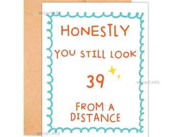 May include: A white birthday card with the text "HONESTLY YOU STILL LOOK 39 FROM A DISTANCE" in orange and blue. The card has a blue scalloped border and a gold star. It is set against a brown envelope.