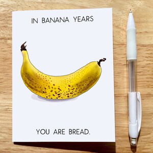 May include: A greeting card with a yellow banana with brown spots and the text "IN BANANA YEARS YOU ARE BREAD."