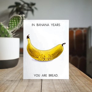May include: A white card with the text "IN BANANA YEARS YOU ARE BREAD."  A cartoon illustration of a yellow banana with brown spots is in the center of the card.