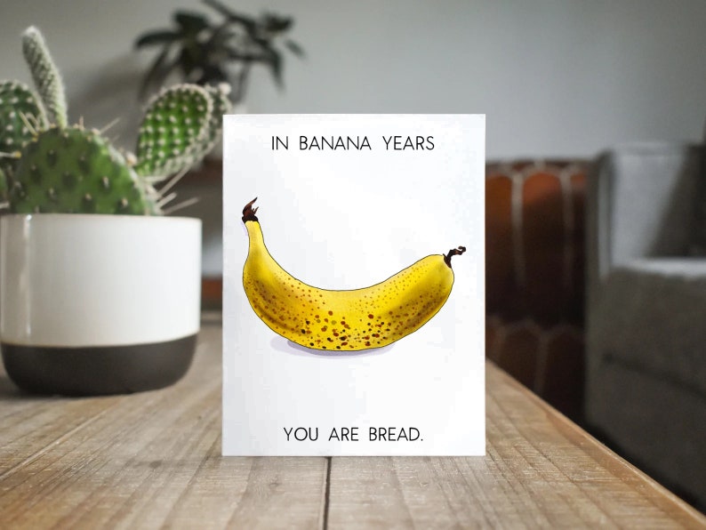 May include: A white card with the text "IN BANANA YEARS YOU ARE BREAD."  A cartoon illustration of a yellow banana with brown spots is in the center of the card.