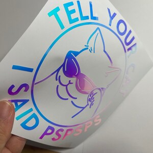 K&ouml;nnte beinhalten: Ein holografischer Aufkleber mit einem blauen, rosa und violetten Farbverlauf. Er zeigt eine Comic-Katze mit Sonnenbrille und dem Text "I said TELL YOUR CAT PSPSPS".