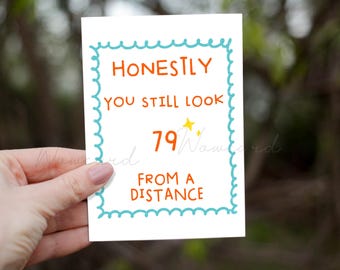 Puede incluir: Una tarjeta de felicitación rectangular blanca con un borde festoneado azul claro. El texto en naranja dice HONESTLY YOU STILL LOOK 79 FROM A DISTANCE. Hay dos pequeños iconos de estrellas amarillas junto al número 79 en la tarjeta.