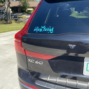 May include: A black Volvo XC60 with a teal blue "stay feral" sticker on the back window.