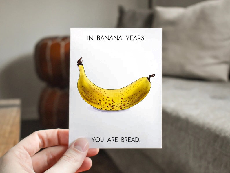 May include: A white card with the text "In banana years, you are bread." and a drawing of a yellow banana with brown spots.