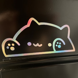 May include: A holographic sticker of a cartoon cat peeking over a surface. The cat's outline is white, with rainbow-colored accents. The sticker is applied to a black surface.