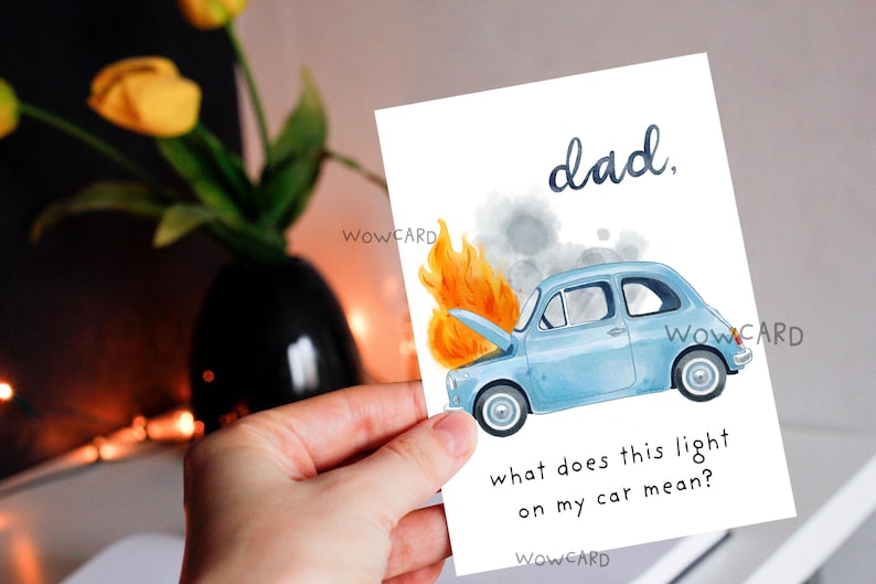May include: A greeting card with a watercolor illustration of a light blue car on fire. The text reads "dad, what does this light on my car mean?" The card is held in a hand.