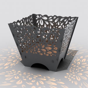 May include: A black metal fire pit with a decorative floral cutout design. The fire pit is sitting on a white surface and casting a shadow of the floral design.