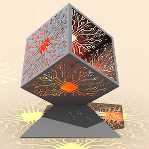 May include: A gray metal cube with a circuit board design cut out. The cube is lit from within, creating a warm orange glow. The cube is sitting on a gray triangular base.