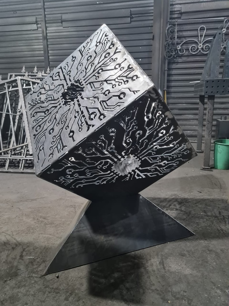 May include: A metal fire pit shaped like a cube with a circuit board design cut out. The fire pit is on a triangular base.