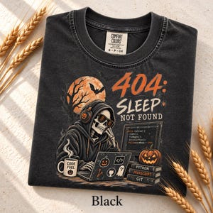Pode incluir: Uma t-shirt preta com um gráfico de um esqueleto a usar auscultadores e óculos de sol enquanto usa um portátil. O texto diz 404: SLEEP NOT FOUND. O design inclui uma lua cheia, uma abóbora e uma caneca com a etiqueta CODE FUEL.