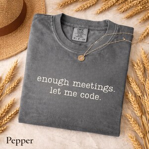 Peut inclure: Un t-shirt à col rond gris anthracite avec le texte blanc "enough meetings. let me code." imprimé sur le devant. Le vêtement présente une étiquette de marque Comfort Colors à l'encolure intérieure et des manches courtes avec une finition délavée.