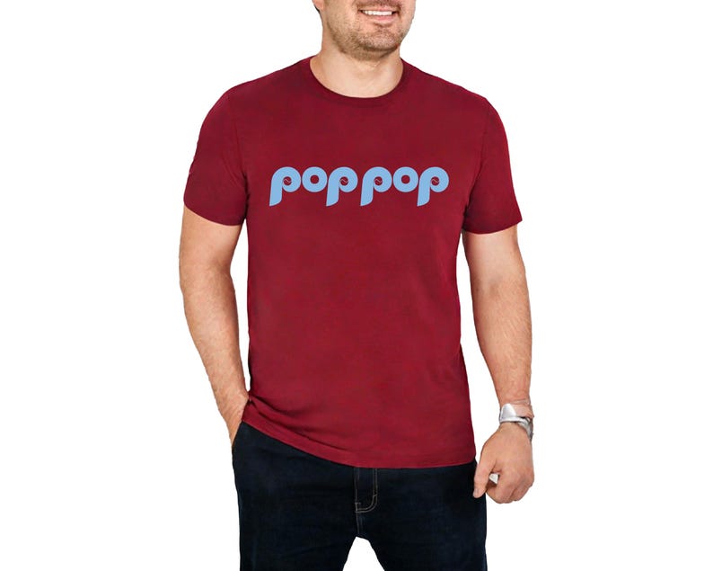 以下が含まれることがあります： ライトブルーの「poppop」という文字が丸みを帯びたフォントでプリントされた、マルーン色のTシャツ。半袖のシャツは人が着ています。その人は濃い青色のジーンズとシルバーの腕時計をしています。