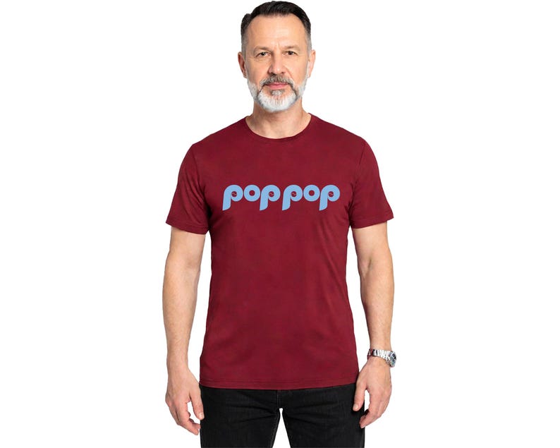 以下が含まれることがあります： 明るい青色の「poppop」という文字がカーブしたデザインの、マルーン色のクルーネックTシャツ。半袖で、人が着ています。その人はシルバーの腕時計と黒いズボンを着用しています。