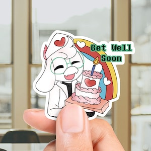 Puede incluir: Una pegatina con un personaje de dibujos animados sosteniendo un pastel con una vela encendida. El personaje es blanco con una marca en forma de corazón y lleva gafas. La pegatina tiene el texto "Get Well Soon" y un arcoíris.