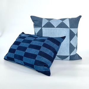 Può includere: Due cuscini quadrati blu. Uno presenta un motivo a scacchiera, l'altro un design geometrico con triangoli e diamanti. I cuscini sono realizzati in tessuto simile al denim. Ideali per un divano.