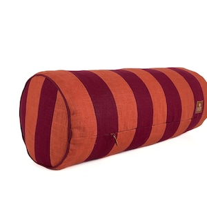 May include: A cylindrical bolster cushion featuring vertical stripes in orange and burgundy. It has a zip closure and a small square label. This cushion is designed for comfort and support, ideal for relaxation.