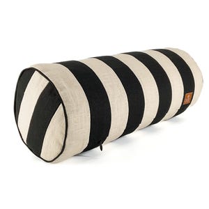 May include: A cylindrical pillow with alternating black and cream-colored stripes. The pillow has a textured appearance and a small, brown leather tag. The ends are rounded and feature a black trim.