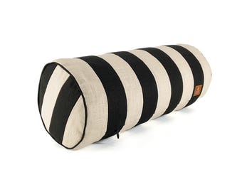 May include: A cylindrical pillow with alternating black and cream-colored stripes. The pillow has a textured appearance and a small, brown leather tag. The ends are rounded and feature a black trim.