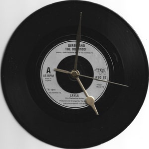 May include: A black vinyl record clock featuring a white label with the text "Derek and the Dominos" and "Layla" with a gold clock hand.