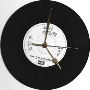 May include: A clock made from a black vinyl record, featuring a white label with the text "IRON MAIDEN" and "CAN I PLAY WITH MADNESS". The clock hands are gold-coloured. A unique decorative item for music lovers.