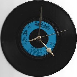 Könnte beinhalten: Eine schwarze Schallplattenuhr mit silbernen Zeigern. Das Plattenlabel ist blau und trägt den Text "SINGLE STONES" und "JUMPIN' JACK FLASH" von "THE ROLLING STONES".