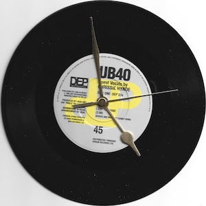 Puede incluir: Un disco de vinilo negro con una etiqueta amarilla. La etiqueta tiene el texto "UB40" y "Guest Vocals by Chrissy Hynde". El disco es un disco de 45 RPM y tiene una aguja de reloj dorada.
