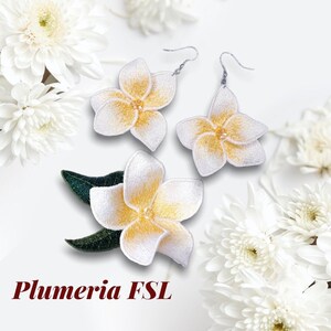 Puede incluir: Un par de pendientes de flores de frangipani bordadas en blanco y amarillo con ganchos plateados. Los pendientes se muestran sobre un fondo blanco con flores blancas.