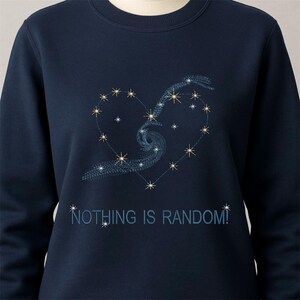 May include: Navy blue sweatshirt with an embroidered heart-shaped constellation design. The design includes stars and a swirling galaxy pattern. The text "NOTHING IS RANDOM!" is embroidered below the heart.