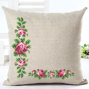 Peut inclure: Un coussin en lin beige avec un motif de broderie florale rose et vert. La broderie présente une rangée verticale de roses et de feuilles sur le côté gauche et une rangée horizontale de roses et de feuilles sur le côté inférieur droit.