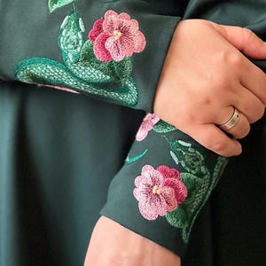 May include: Green long-sleeved dress with pink and green embroidered flowers on the cuffs.