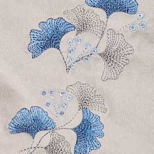 May include: Embroidered design featuring blue and gray ginkgo leaves with small blue circles on stems. The design is on a beige fabric background.