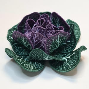 May include: A purple cabbage with green outer leaves, embroidered in detail. The cabbage is a 3D design, with the leaves curled and overlapping.