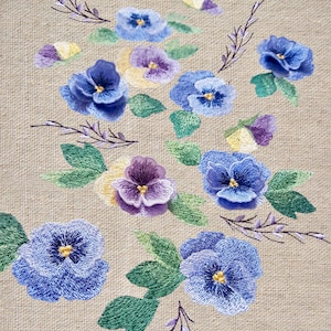 Könnte beinhalten: Gestickte Blumenmuster auf einem beigefarbenen Leinenstoff mit violetten, blauen und gelben Stiefmütterchen mit grünen Blättern und Stielen.