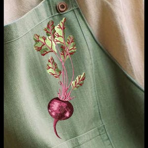 Puede incluir: Un delantal verde con una remolacha bordada en rojo y verde con hojas.