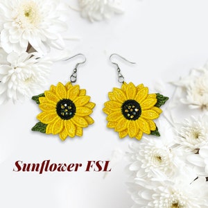 Peut inclure: Une paire de boucles d'oreilles en forme de tournesol avec des feuilles vertes et un centre en strass. Les boucles d'oreilles sont en tissu jaune et vert et ont des crochets argentés.