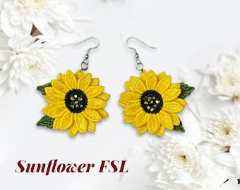Puede incluir: Un par de pendientes de girasol con hojas verdes y un centro de strass. Los pendientes están hechos de tela amarilla y verde y tienen ganchos plateados.