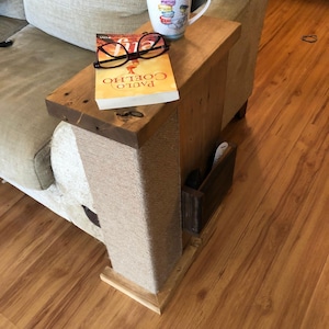 May include: A rustic wooden side table with a built-in storage compartment. The table features a book, eyeglasses, and a mug with a colorful design. The base is wrapped in natural rope. The table is placed next to a beige sofa.