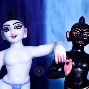 May include: Two statues of figures with stylized features. One is white with a blue thong, the other is black. Both have black hair, pink lips, and detailed facial features. The background is a gradient of blue.