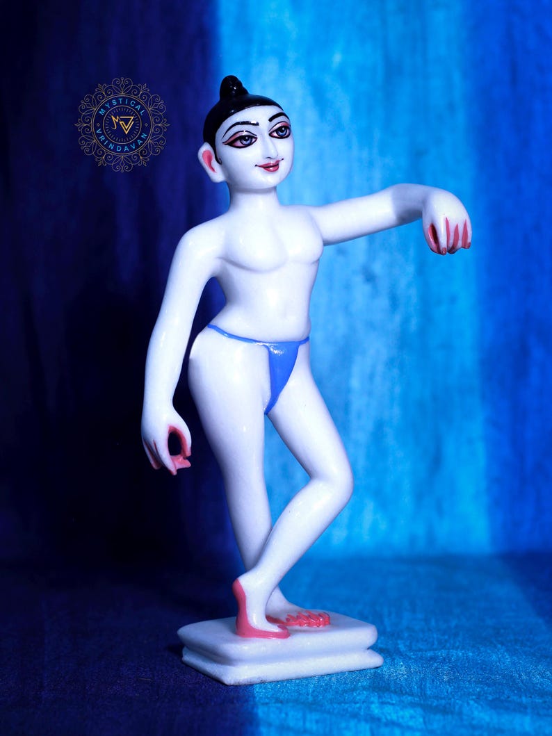 May include: A white figurine of a person in a dancing pose, with black hair and facial features. The figurine wears a blue thong and has pink accents on the hands and feet. It stands on a white rectangular base against a blue backdrop.