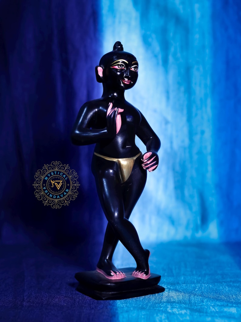 May include: A black figurine of a person with pink accents on the hands and feet, and gold accents on the waist. The figurine is standing on a black base, with a blue and white background. The figurine has a gold-colored waist covering.