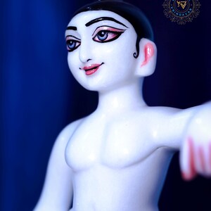 May include: A white figurine of a person with black hair and painted facial features, including blue eyes and pink lips. The figure is wearing a blue garment and has a muscular physique. The background is a deep blue.