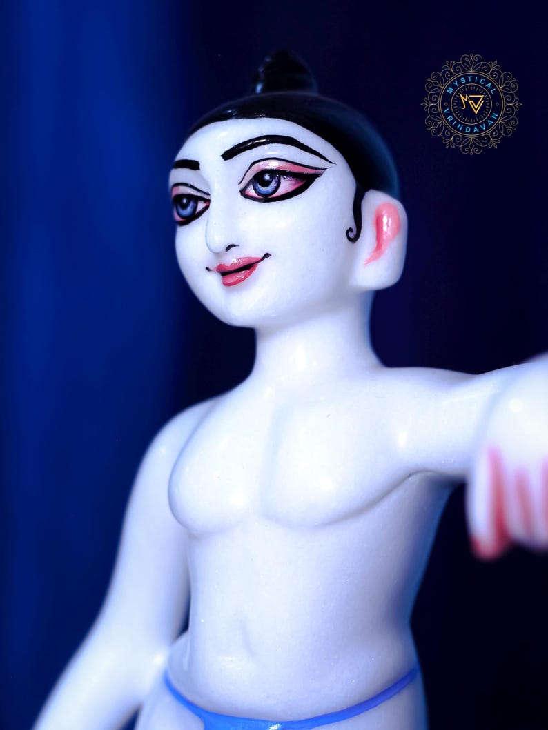May include: A white figurine of a person with black hair and painted facial features, including blue eyes and pink lips. The figure is wearing a blue garment and has a muscular physique. The background is a deep blue.
