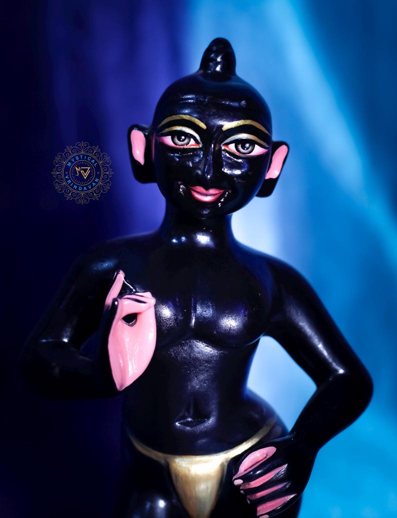 May include: A glossy black figurine of a person with gold accents on the eyes and a gold loincloth. The ears and hands are painted pink. The figure is posed with one hand raised and the other resting on the hip.