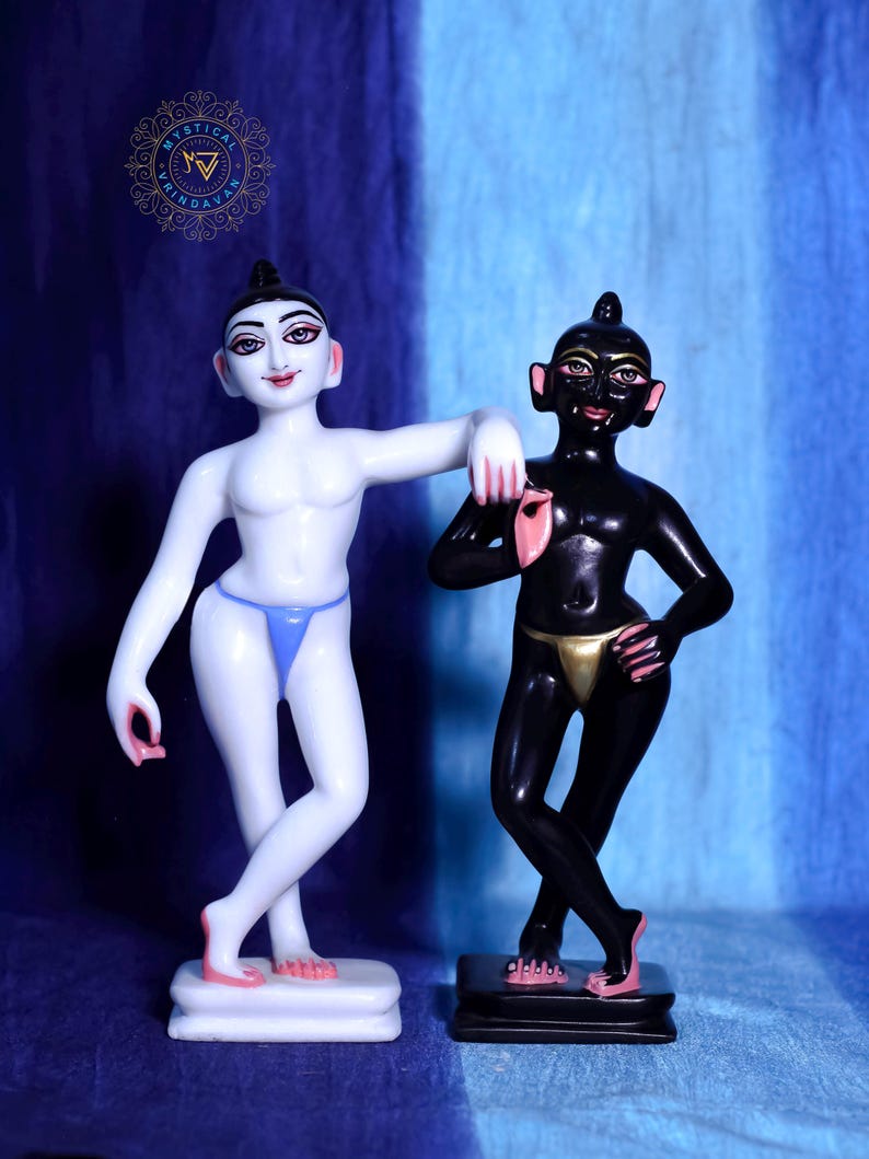 May include: Two statues of human figures. One is white with a blue thong, the other is black with a gold thong. Both have dark hair and are standing on small rectangular bases. The background is blue.