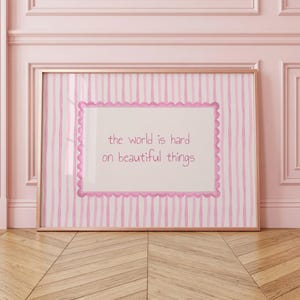 Peut inclure: Une &oelig;uvre d'art murale encadr&eacute;e rectangulaire avec un fond &agrave; rayures verticales rose clair et blanc. Au centre, un panneau rectangulaire blanc avec une bordure rose festonn&eacute;e affiche le texte : the world is hard on beautiful things.