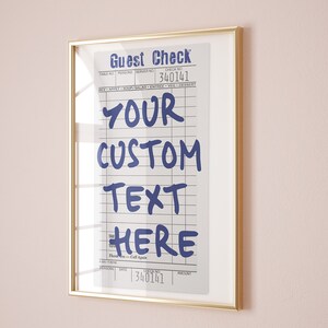 May include: A framed wall art print featuring a vintage-style guest check design with blue text that reads Guest Check, 340141, YOUR CUSTOM TEXT HERE, and Thank You - Call Again. The print is enclosed in a thin, metallic gold-colored rectangular frame.