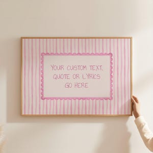 May include: A rectangular wall art print in a light wooden frame featuring a pink and white vertical striped background. In the center, a white rectangular label with a scalloped pink border displays the text: YOUR CUSTOM TEXT, QUOTE OR LYRICS GO HERE.