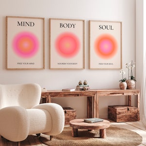 May include: Three framed art prints with the words "MIND", "BODY", and "SOUL" in black text. Each print features a vibrant, circular gradient in shades of pink, orange, and yellow. The text "FREE YOUR MIND", "NOURISH YOUR BODY", and "FEED YOUR SOUL" are below.