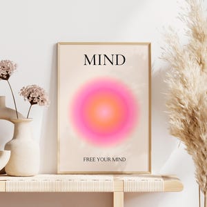 May include: A framed art print with the word "MIND" at the top and "FREE YOUR MIND" at the bottom. The artwork features a vibrant pink and orange gradient circle. Decorative vases and dried flowers are in the foreground.